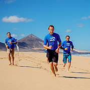surfdeelnemers joggen over een lang zandstrand om op te warmen voor de surfles