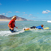 surfers lopen met hun boards het water in om golven te pakken tijdens de surfcursus