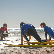 surfcoach legt op het strand uit hoe je een take-off uitvoert vóór het ingaan van het water