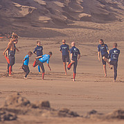 ouders en kinderen doen samen opwarmoefeningen op het zand voor de surfles voor gezinnen
